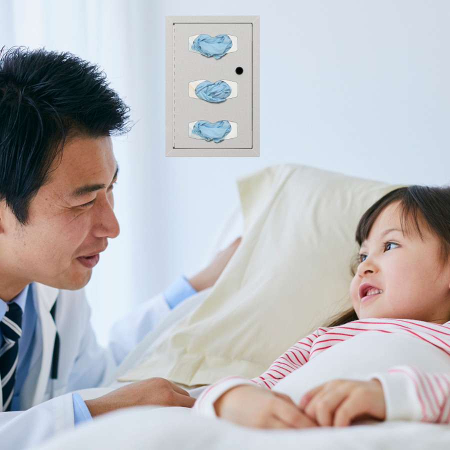 Asian male doctor at bedside of pediatric patient. behind them is an ORIGIN triple glove dispenser on the wall.